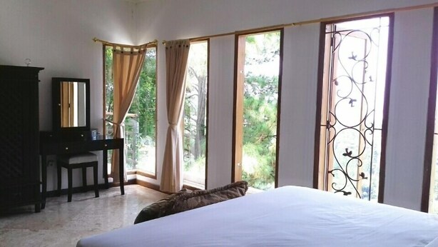A bedroom with a bed, a desk, and a chair. There are large windows with curtains and a metal gate. - De Bukit Dago Villa by HouseinBandung (Bandung)