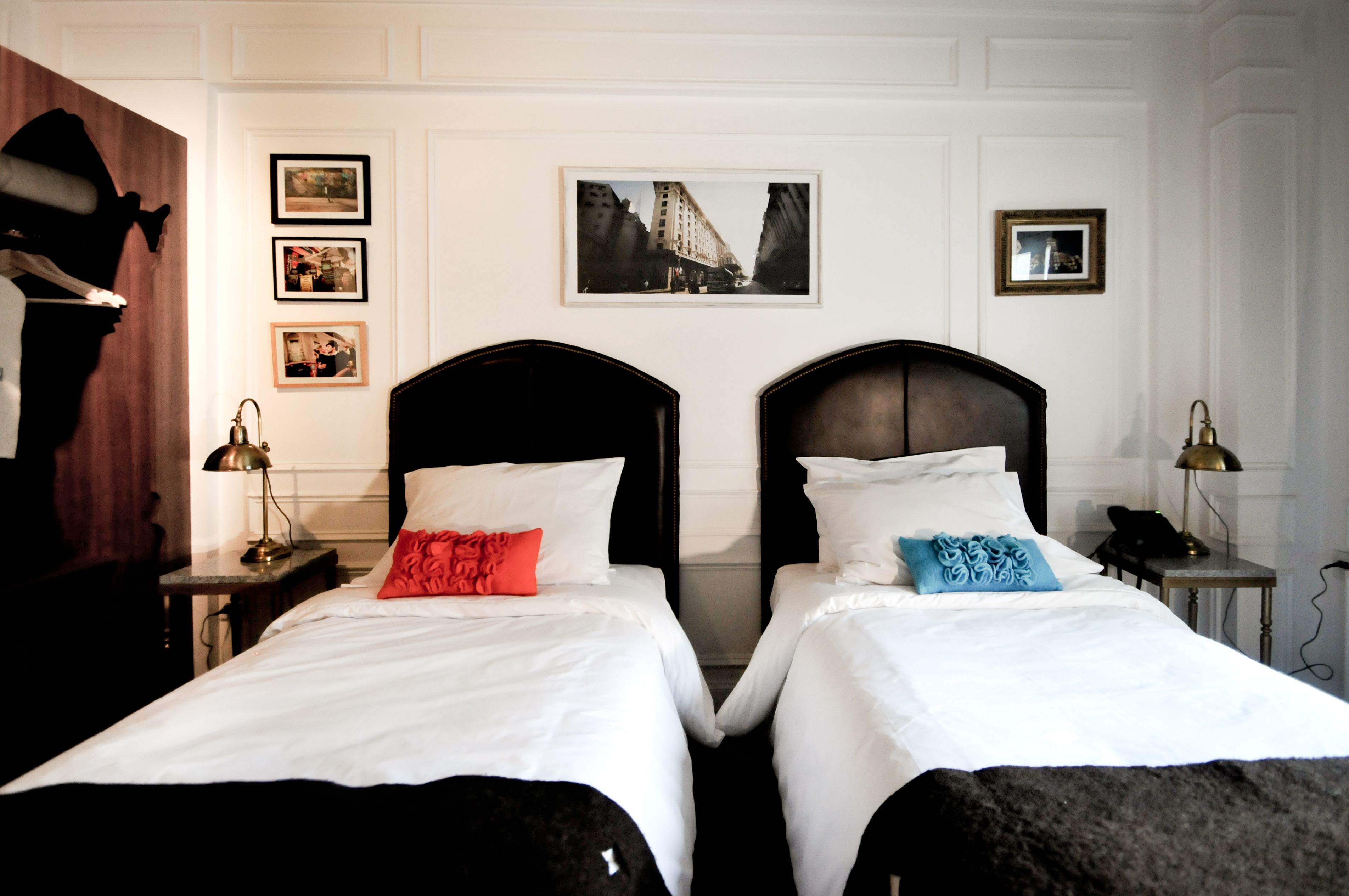Een hotelkamer met twee bedden, een nachtkastje met een lamp en ingelijste foto’s aan de muur.