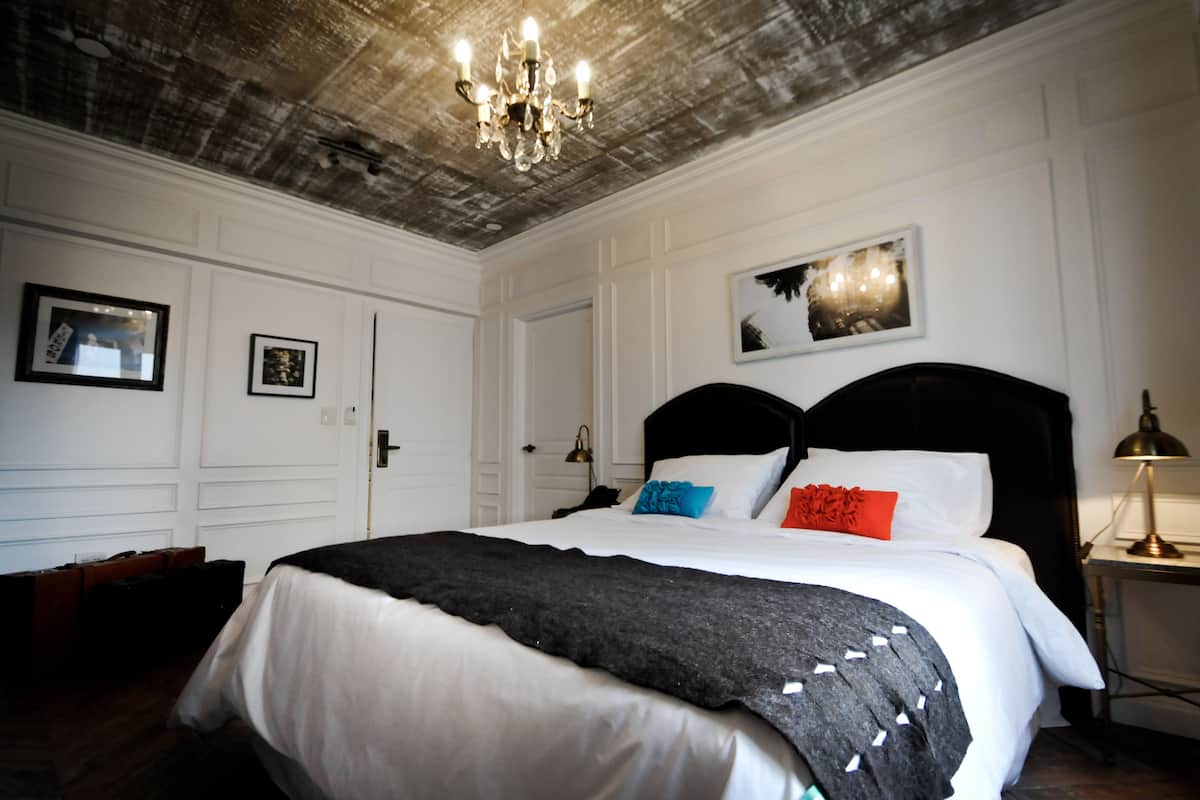 Una habitación de hotel con una cama grande, una araña y cuadros enmarcados en la pared.
