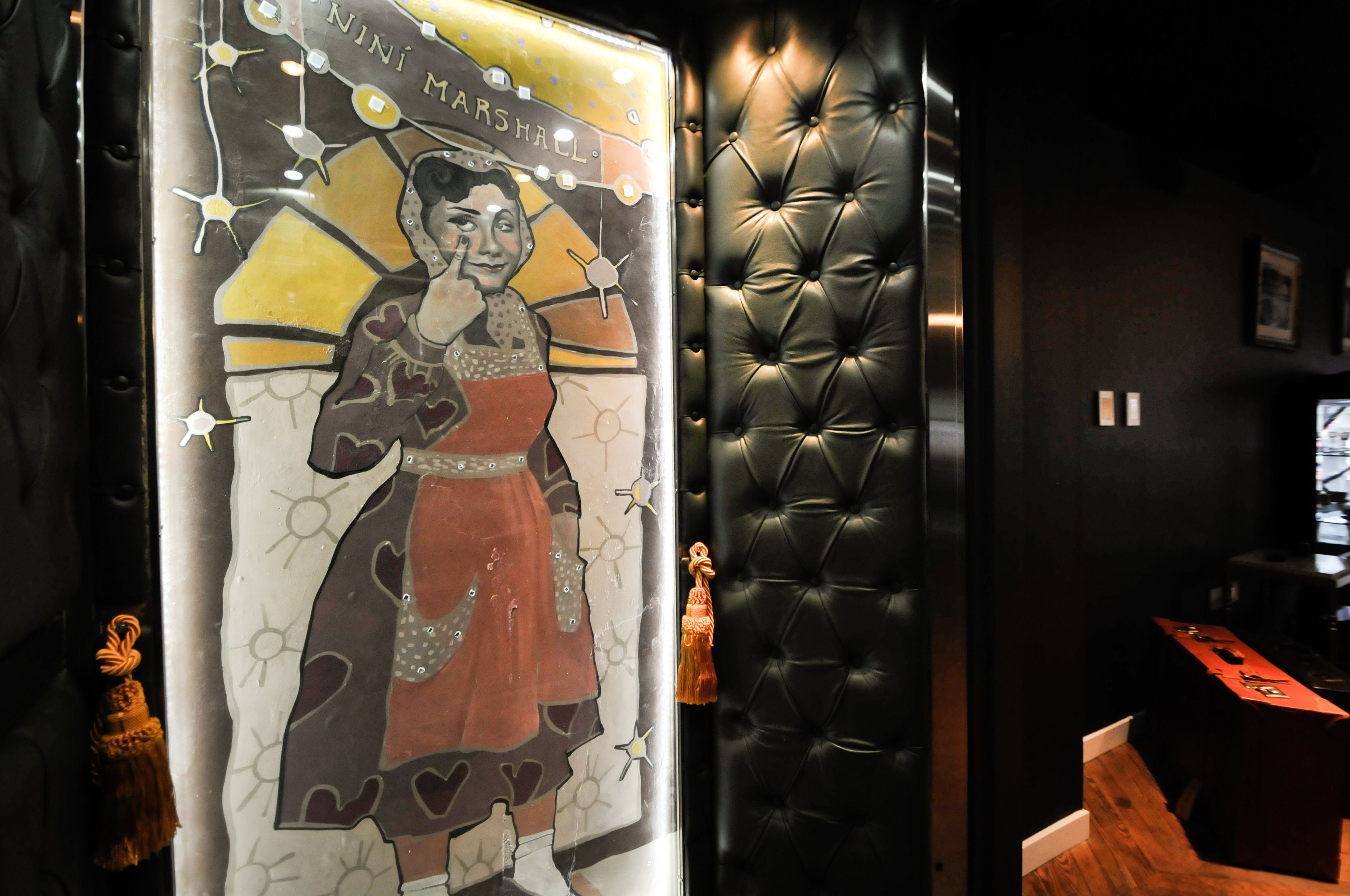 A room with a tufted leather wall, a poster with a woman in a dress, and a small statue.