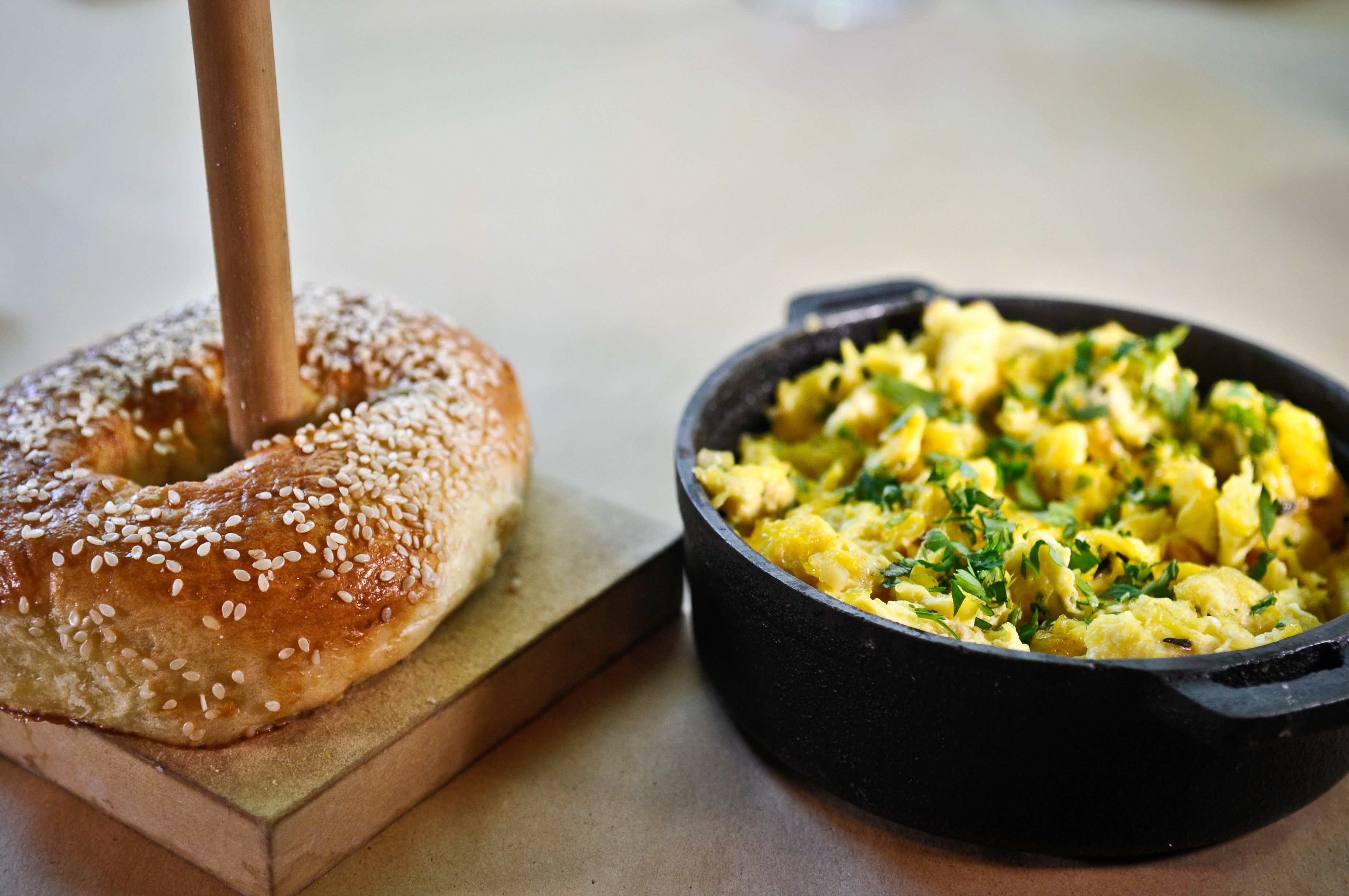 A breakfast setting with a bagel topped with sesame seeds and a skillet of scrambled eggs.