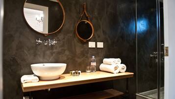 A modern bathroom with a large oval mirror, a round mirror, a wooden vanity with a bowl sink, and a glass-enclosed shower.