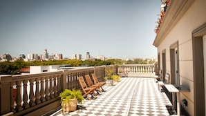 A rooftop terrace with a checkered floor, wooden chairs, potted plants, and a city view. - Hotel Clasico (Buenos Aires)