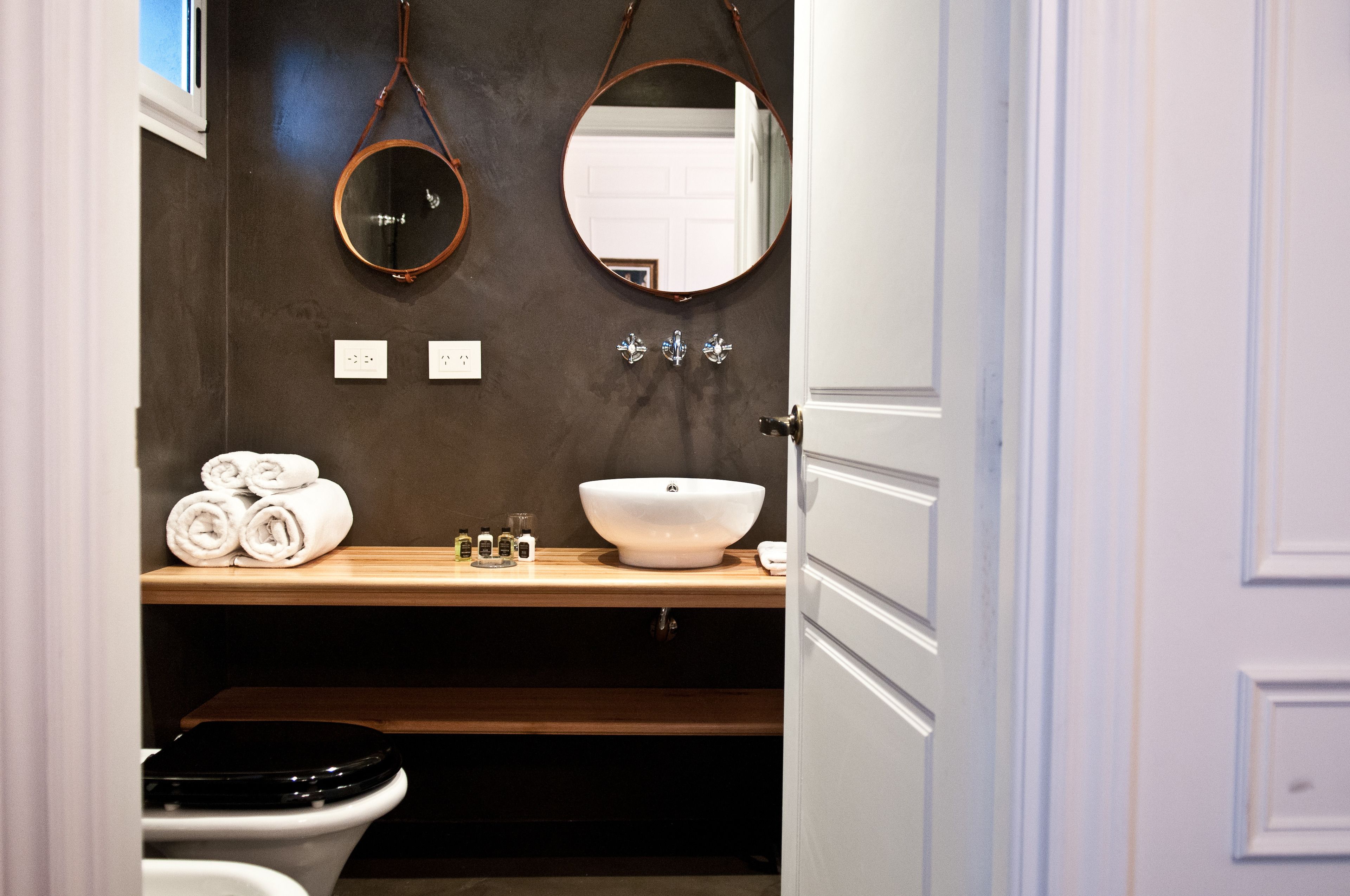 A bathroom with a wooden vanity, a white sink, and two mirrors.