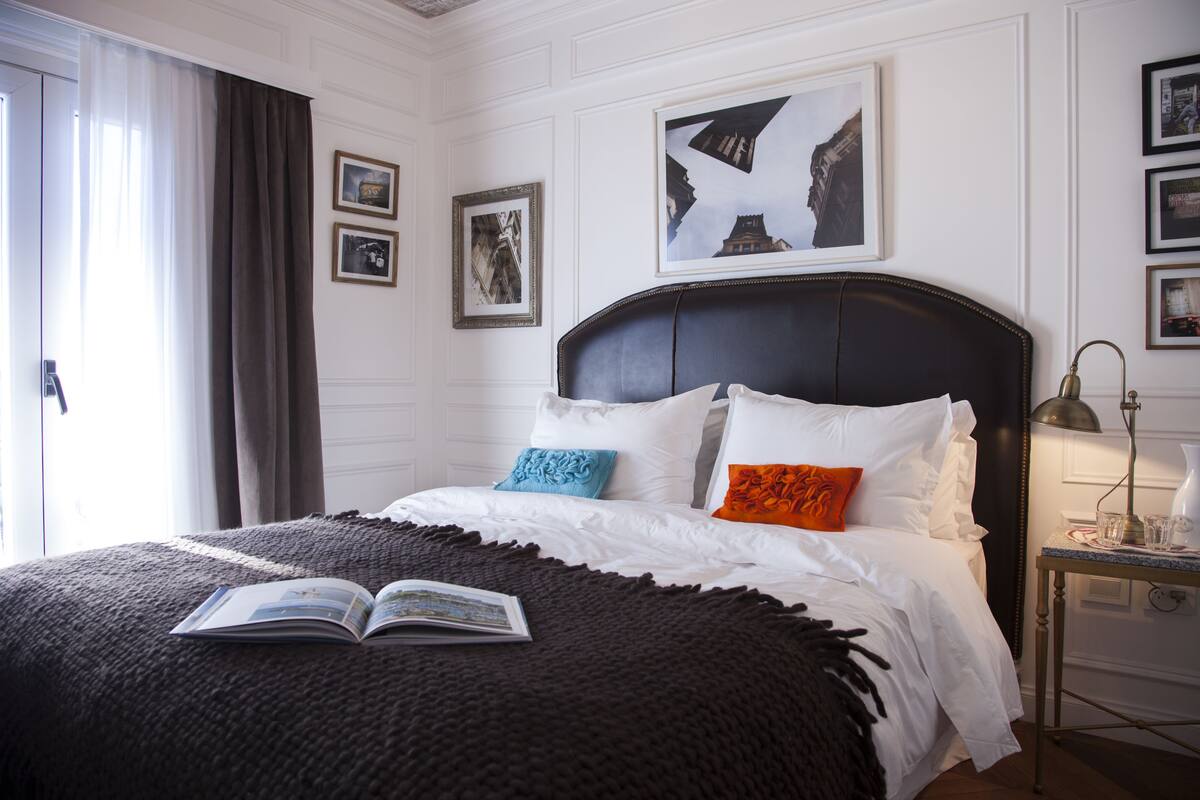 Un cuarto de hotel con una cama grande, una mesita de noche con una lámpara y cuadros enmarcados en la pared.