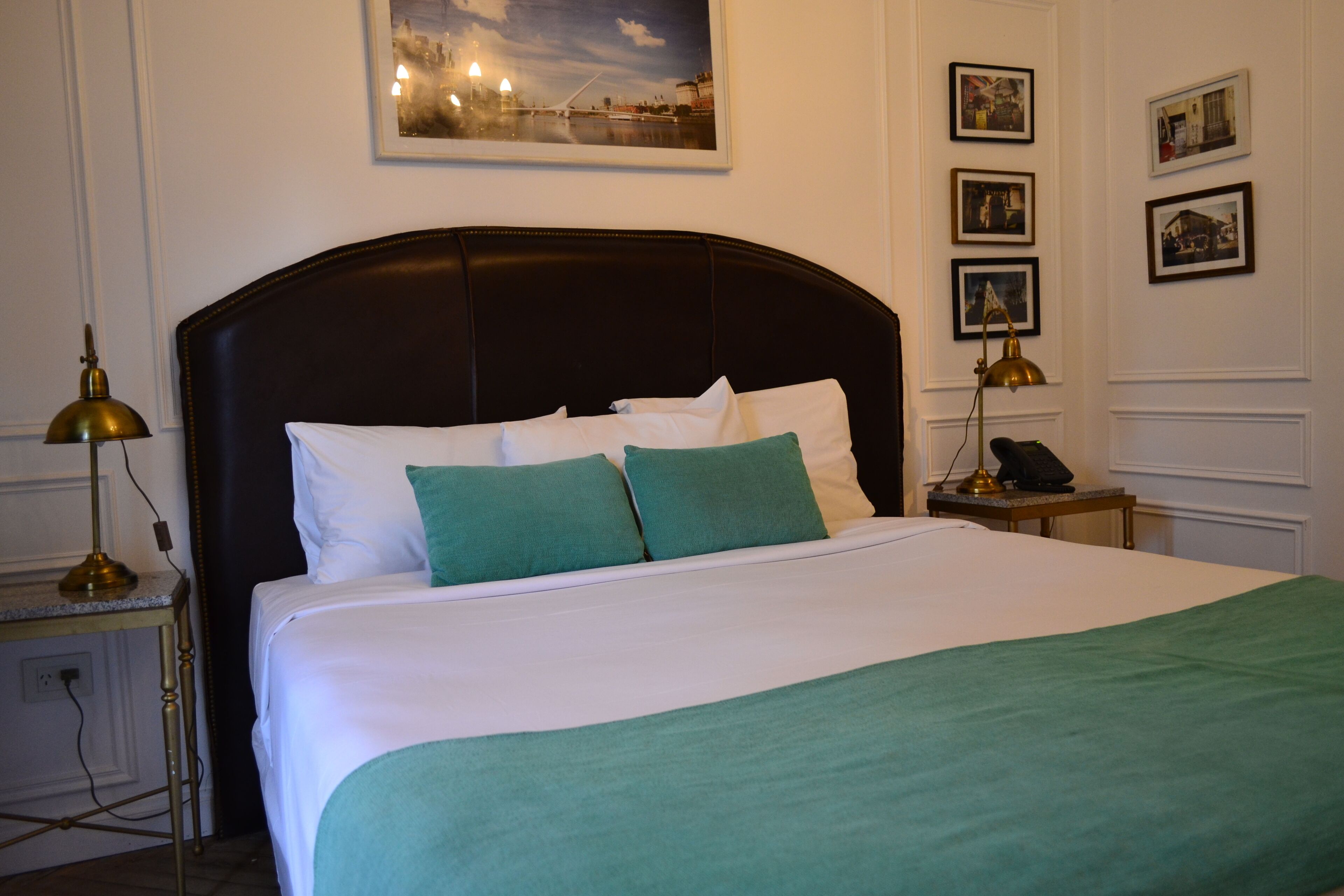 A neatly made bed with white and green bedding, a dark headboard, and a nightstand with a lamp.