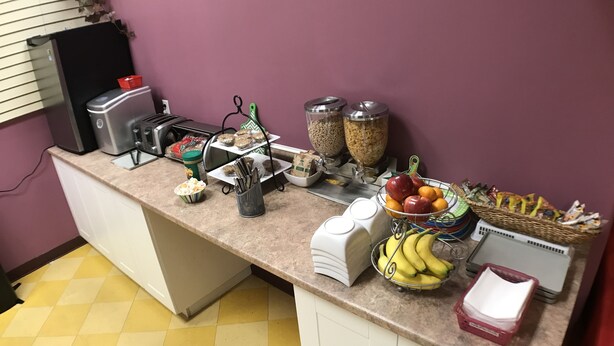 A breakfast bar with a coffee machine, cereal, and fruit. - Balsam Suites Boutique Inn & Residence (Timmins)