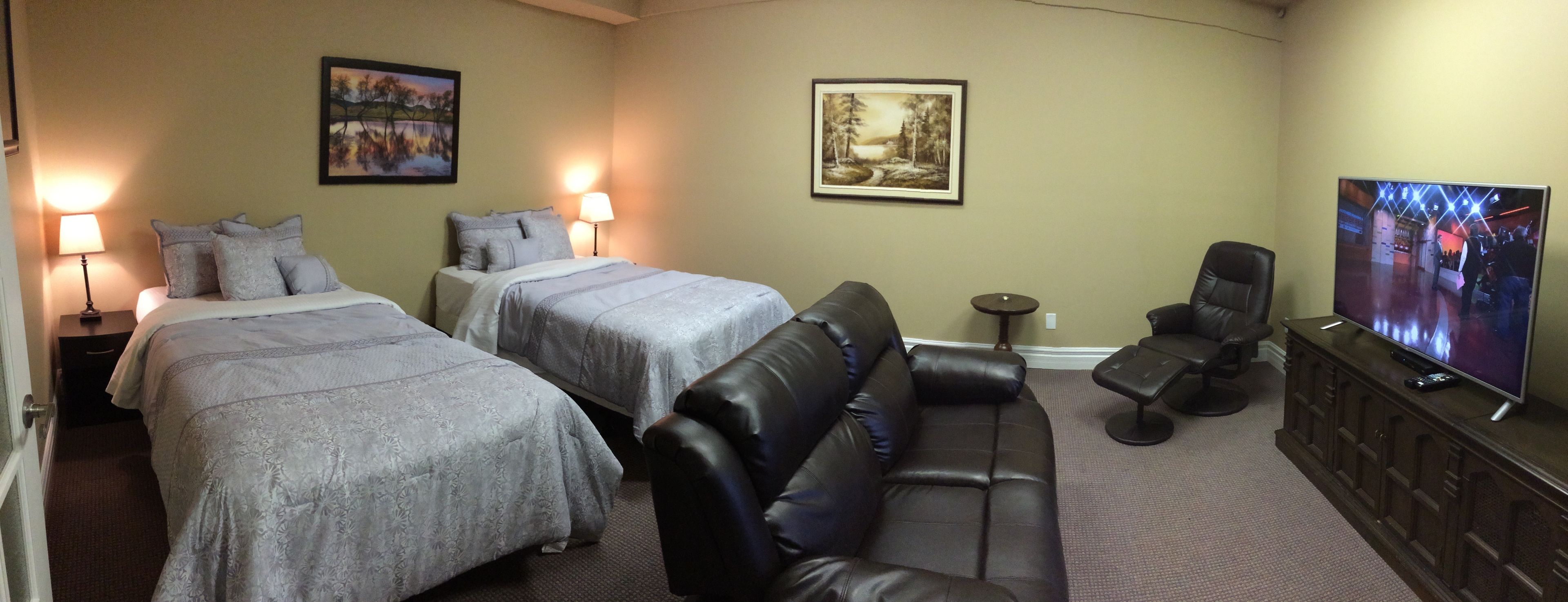 A hotel room with two beds, a leather sofa, a TV, and artwork on the walls.