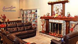 A living room with a fireplace, leather sofas, a bookshelf, and a decorative mantelpiece. - Balsam Suites Boutique Inn & Residence (Timmins)