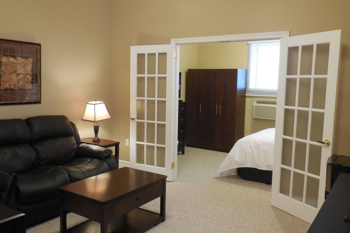 A hotel room with a leather sofa, a small table, a lamp, a bed, and a wardrobe.