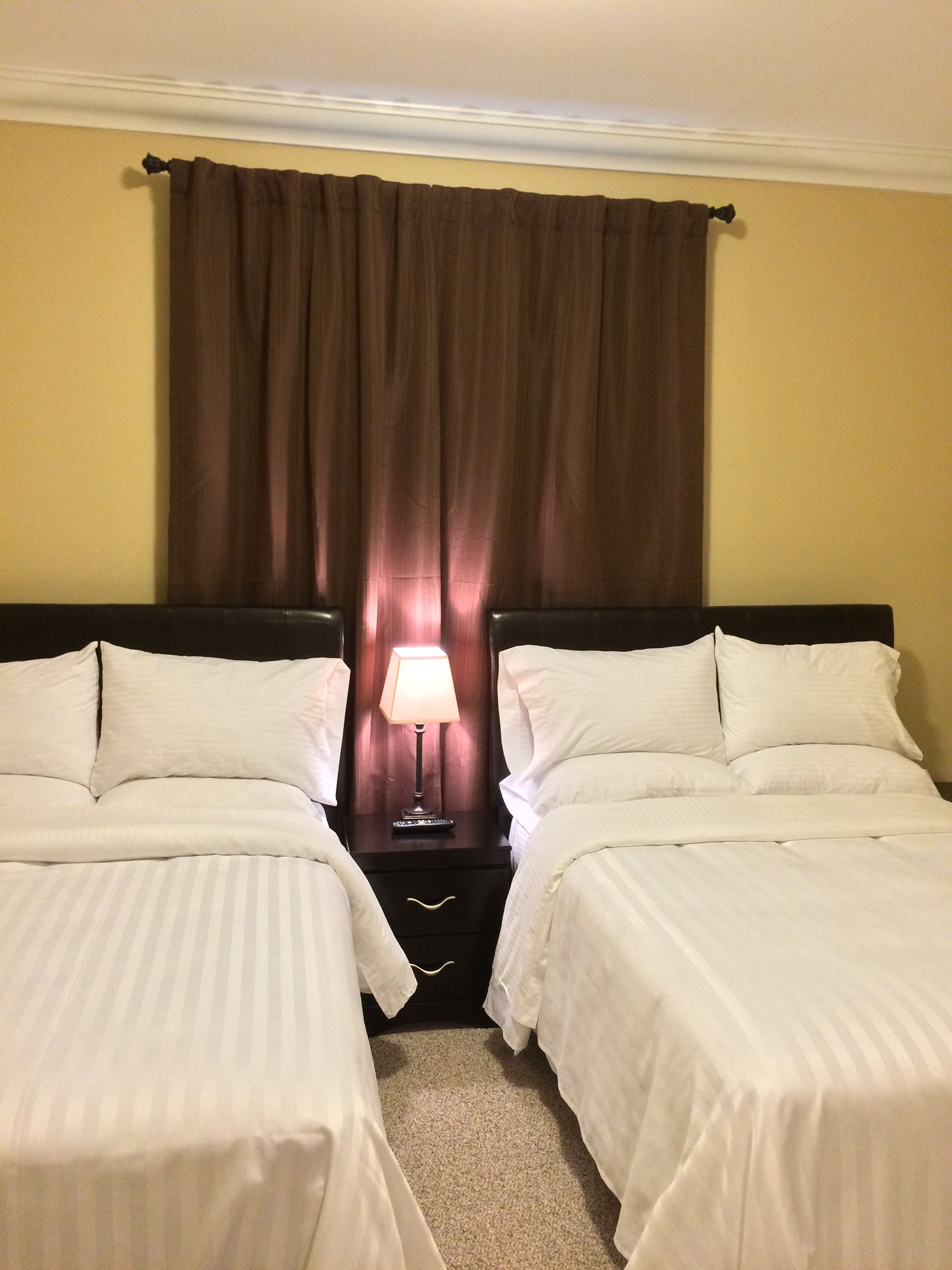 Una habitación de hotel con dos camas, una mesita de noche con lámpara y una cortina marrón.