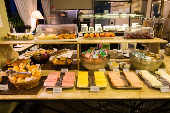 Un bufé con diversas opciones de comida, entre ellas frutas, quesos y pasteles.