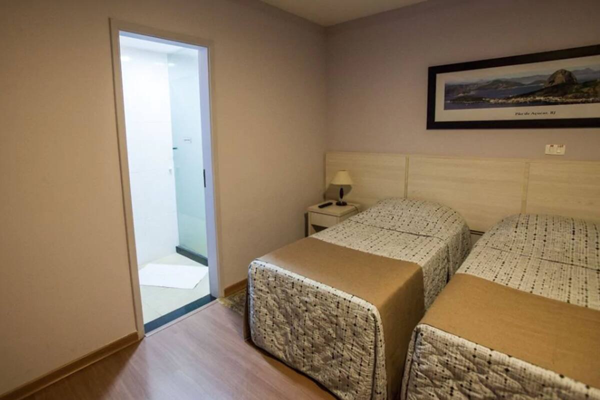 Une chambre d’hôtel avec deux lits, une table de chevet, un tableau encadré au mur et une porte donnant sur un balcon.