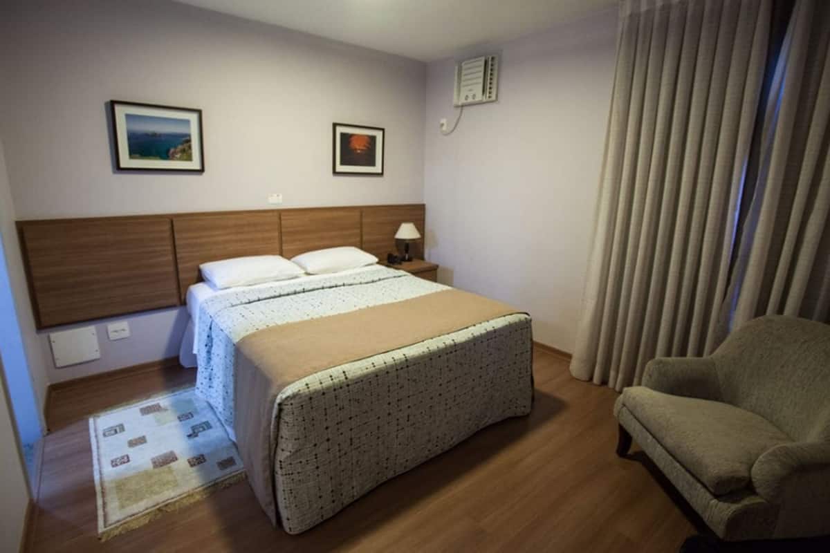 Une chambre d’hôtel avec un lit, une chaise, une table de chevet et deux tableaux encadrés au mur.