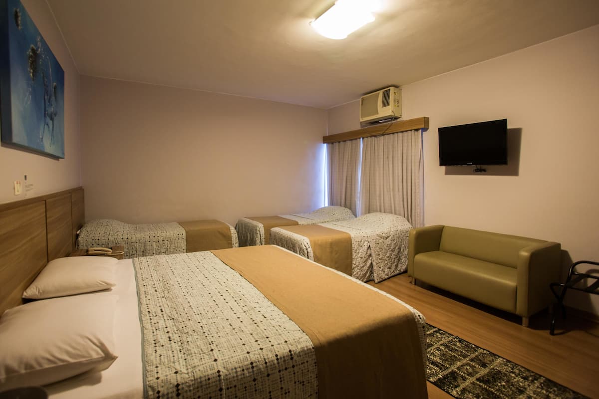 Une chambre d’hôtel avec deux lits, un canapé, une télévision et un appareil de climatisation.