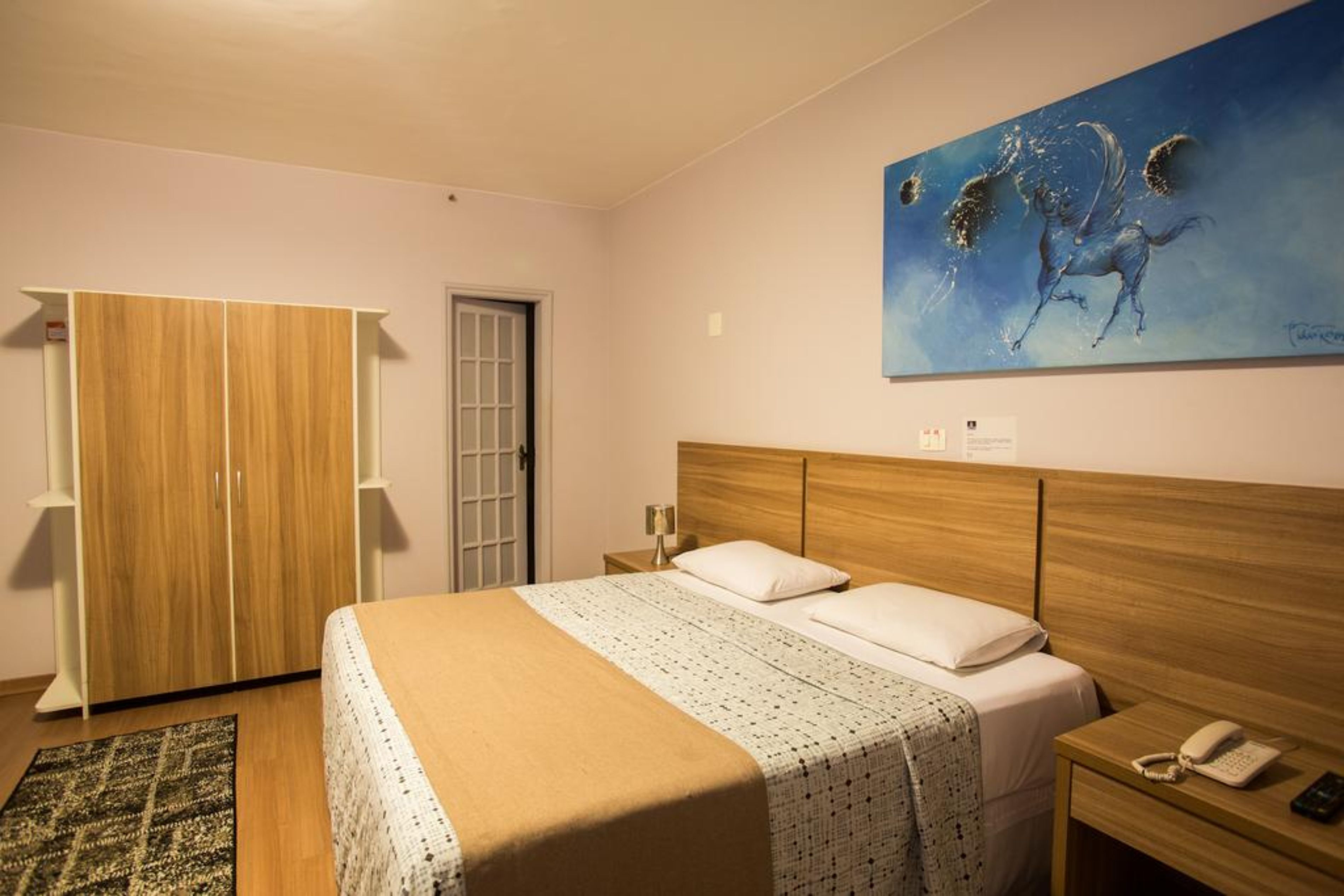 A bedroom with a wooden bed, a nightstand, a telephone, and a painting on the wall.