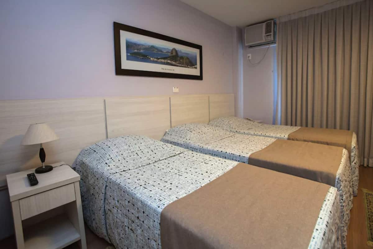 Une chambre d’hôtel avec deux lits, une table de chevet avec une lampe, un tableau encadré au mur et un appareil de climatisation.