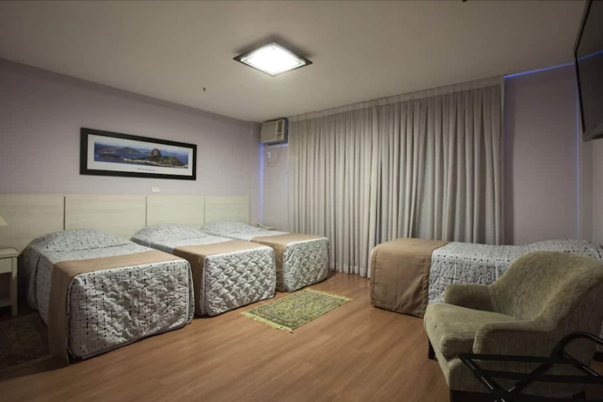 Une chambre d’hôtel avec deux lits, une chaise, un téléviseur à écran plat, un tableau encadré au mur et une fenêtre avec des rideaux.