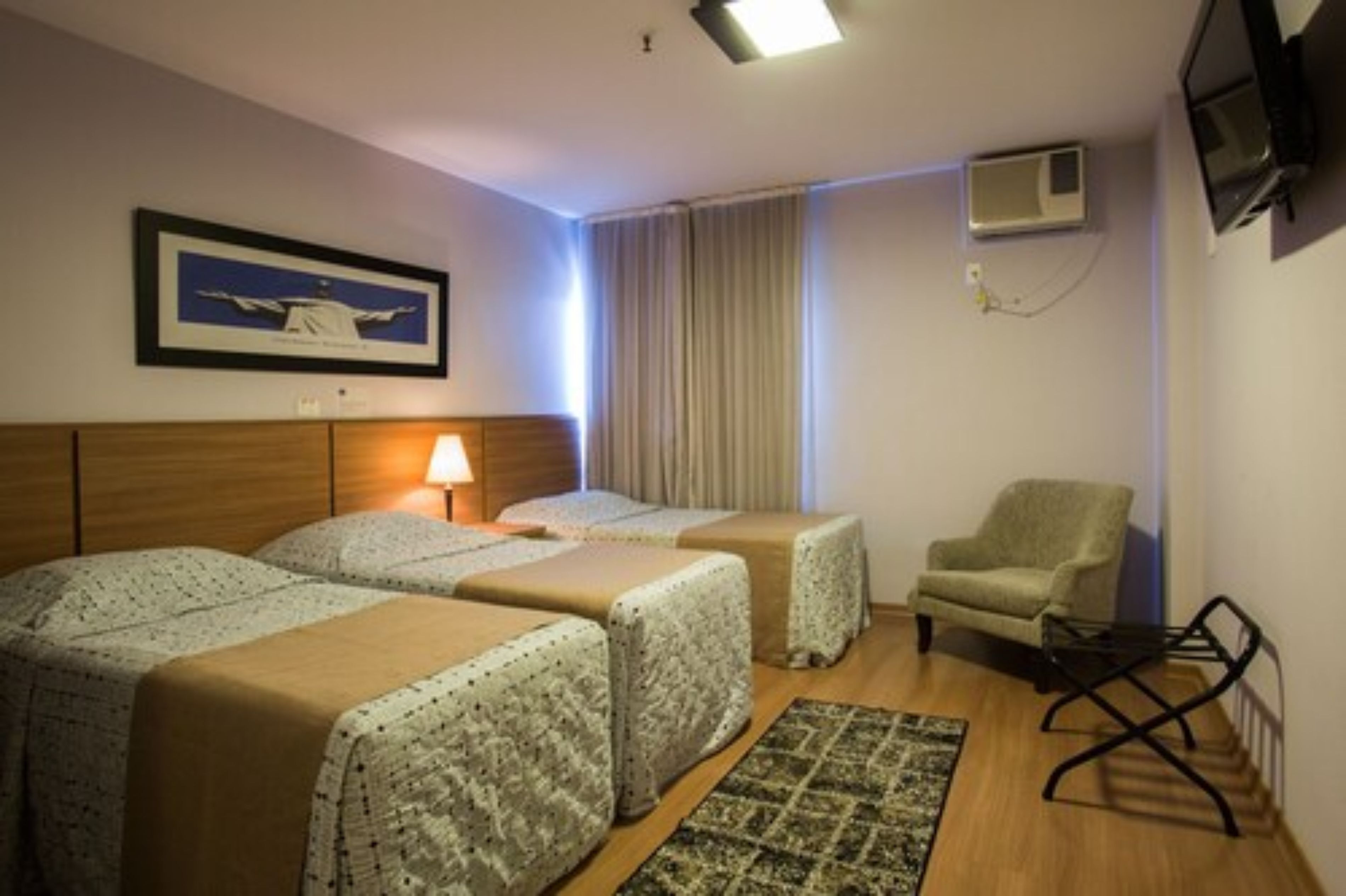 Ein Hotelzimmer mit zwei Betten, einem Sessel, einem Fernseher und einem gerahmten Bild an der Wand.