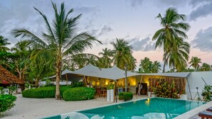 A poolside area with a clear pool, palm trees, and a covered seating area. - Indigo Beach Zanzibar (Bwejuu)