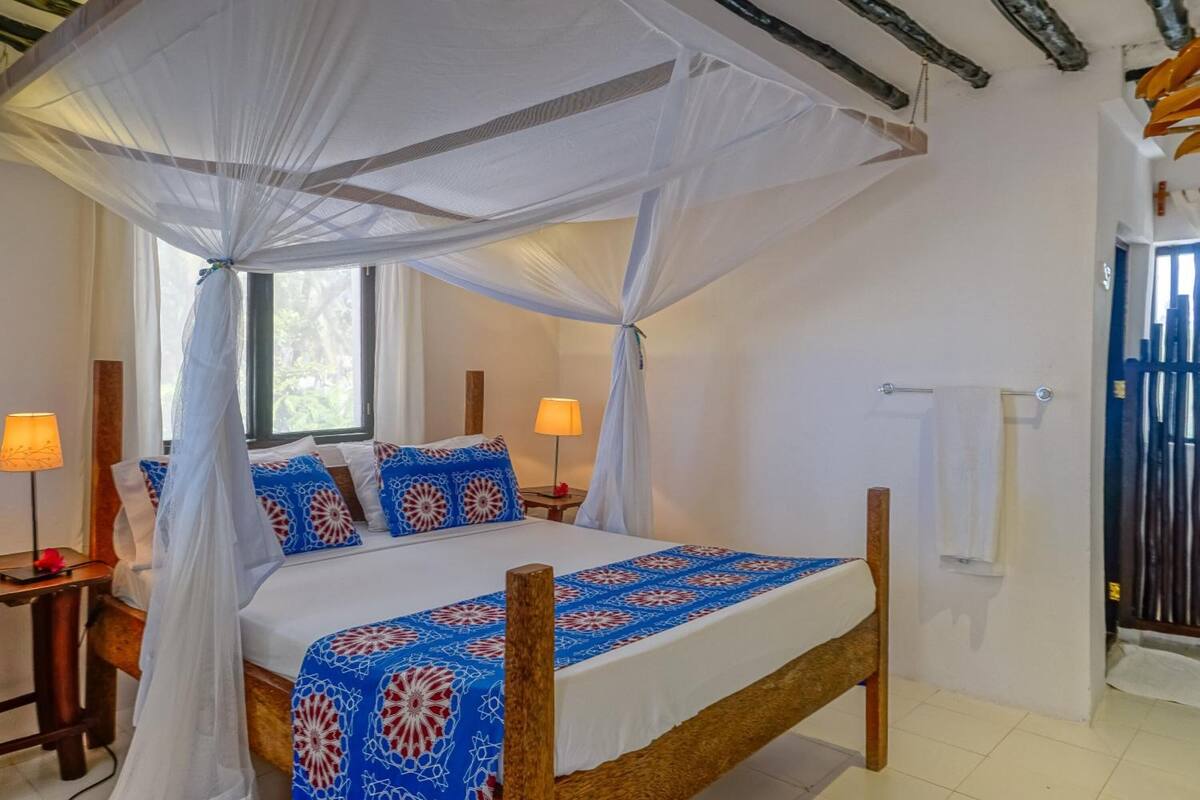 A bedroom with a canopy bed, two bedside lamps, and a view of the outdoors through a window.