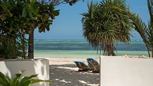 A beach with two lounge chairs and a palm tree, overlooking a clear blue sea. - Indigo Beach Zanzibar (Bwejuu)