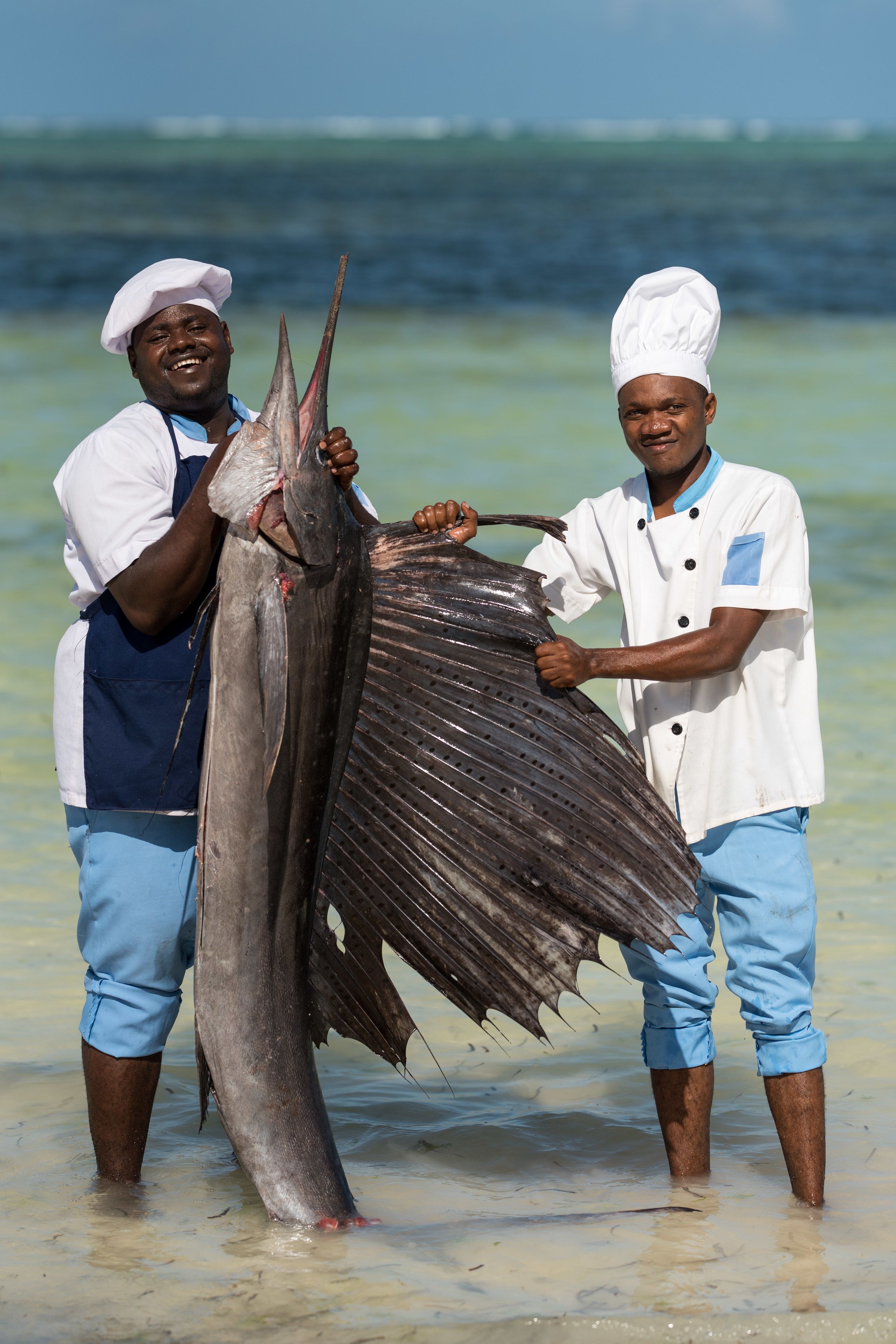 Two individuals holding a large fish in shallow water.