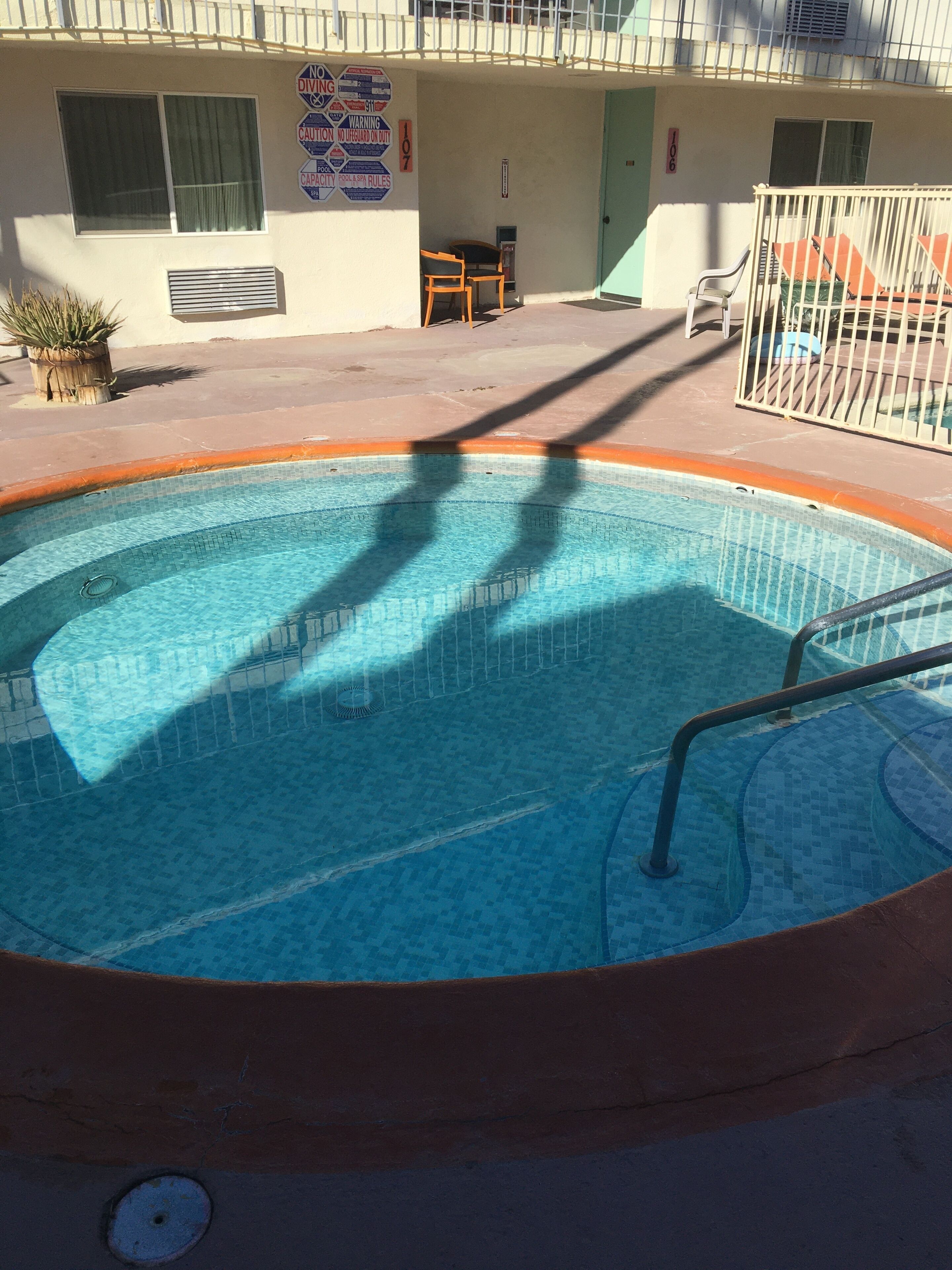 A swimming pool with a metal railing, a chair, and a table outside a building with a signboard.