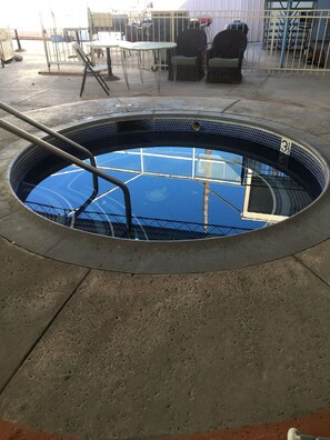 A circular swimming pool with a metal ladder, surrounded by concrete flooring and wicker chairs. - Sandpiper Springs Spa & Retreat (Desert Hot Springs)