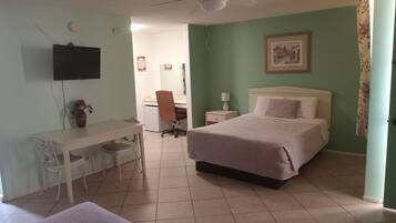 A hotel room with a bed, a desk, a chair, a television, and a ceiling fan.