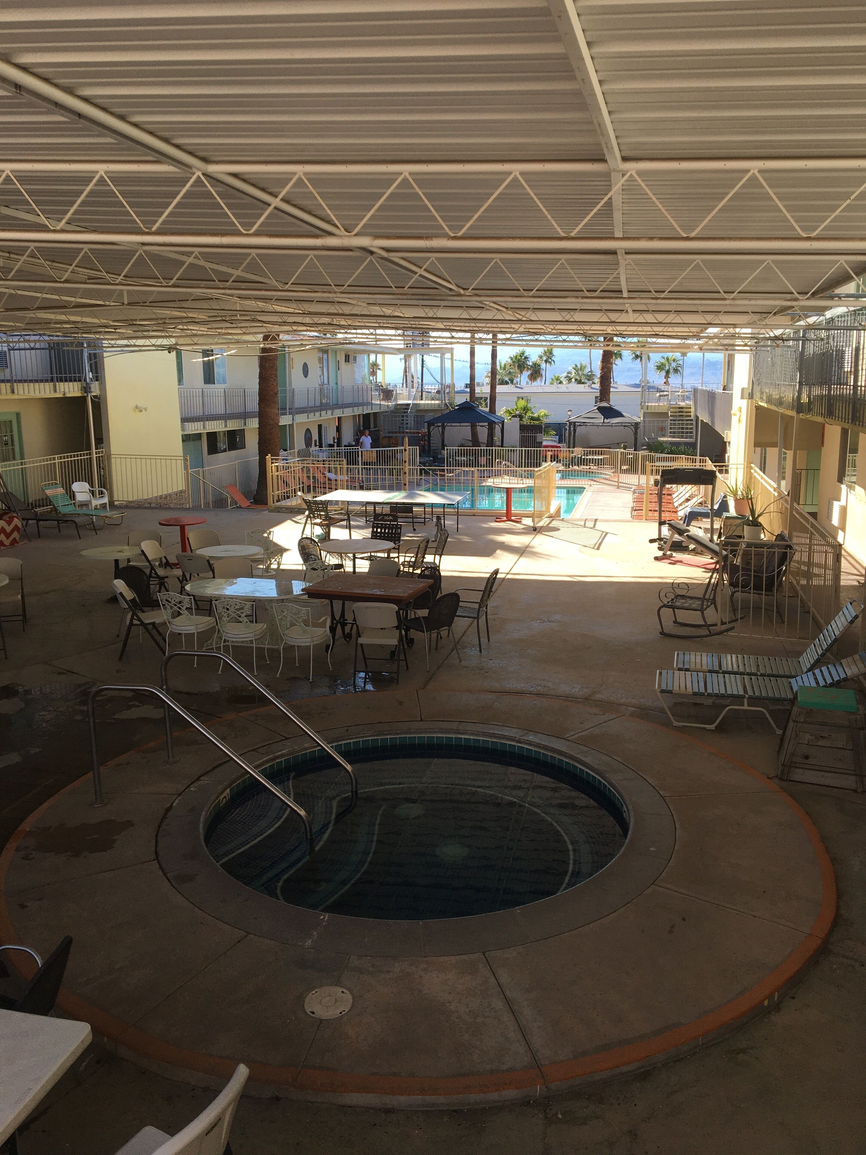 Un espace extérieur abrité avec une piscine, des chaises longues et des tables, le tout entouré de murs hauts et agrémenté de poutres métalliques.
