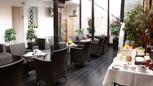 Un espace extérieur aménagé pour les repas, avec des meubles en osier, une table recouverte d’une nappe blanche et des plantes en pot.
