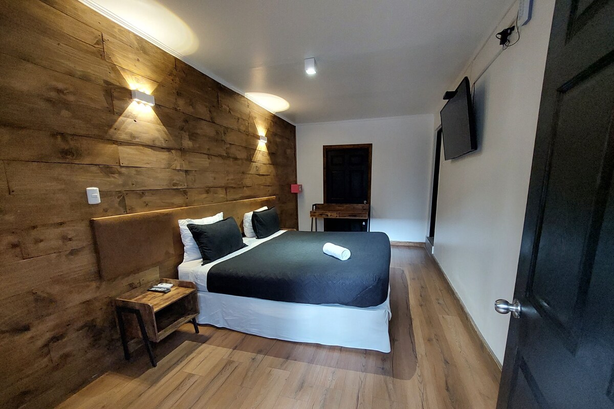 Ein Schlafzimmer mit Holz-Kopfteil, einem Bett mit weißer und schwarzer Bettwäsche, einem Nachttisch und Holzboden.