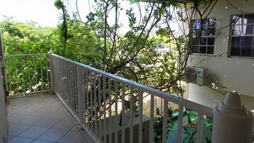 A balcony with a white railing, a tiled floor, and a view of greenery and a building in the background.
