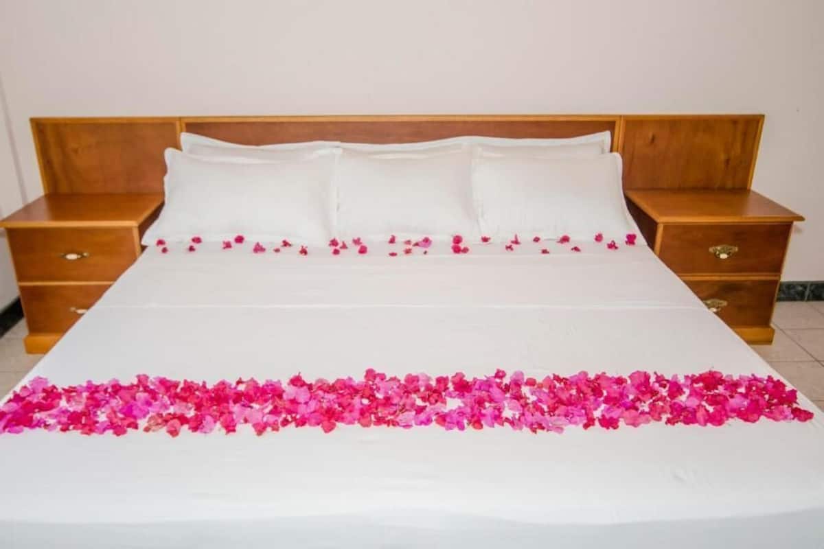 A neatly made bed with white linens and pink flower petals arranged at the foot of the bed.