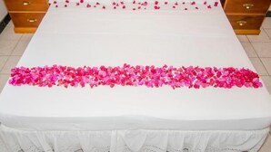 A bed with white linens, pink flower petals on the bedspread, and wooden nightstands with drawers.
