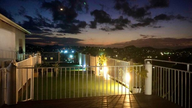 A nighttime view of a balcony with a metal railing, a white pillar, and a distant cityscape with lights.