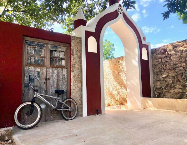 A bicycle parked outside a building with a red and white facade, a stone wall, and a clear sky. - Hotel Posada San Juan (Valladolid)