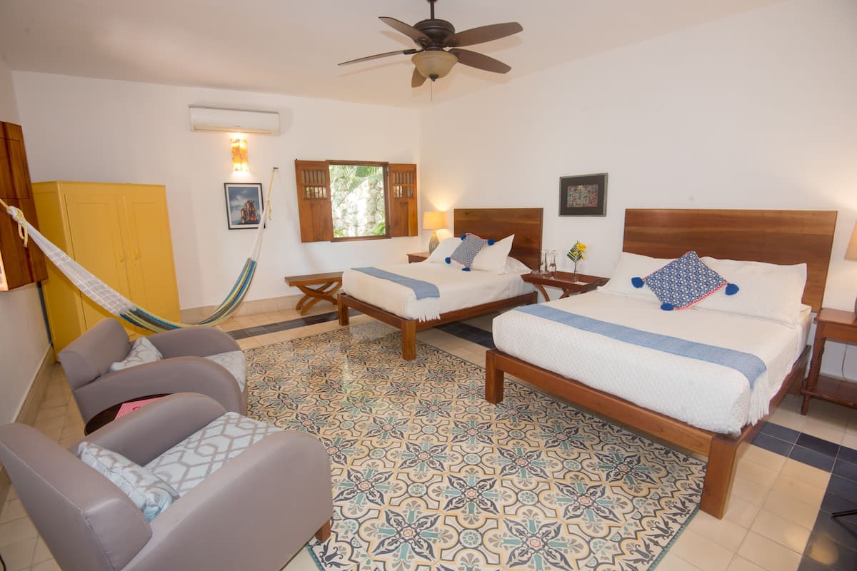 Quarto de hotel com duas camas, uma rede, uma cadeira e piso estampado.