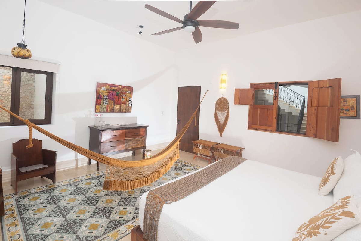 Um quarto com uma cama, uma rede, uma escrivaninha, uma cadeira e uma escada.