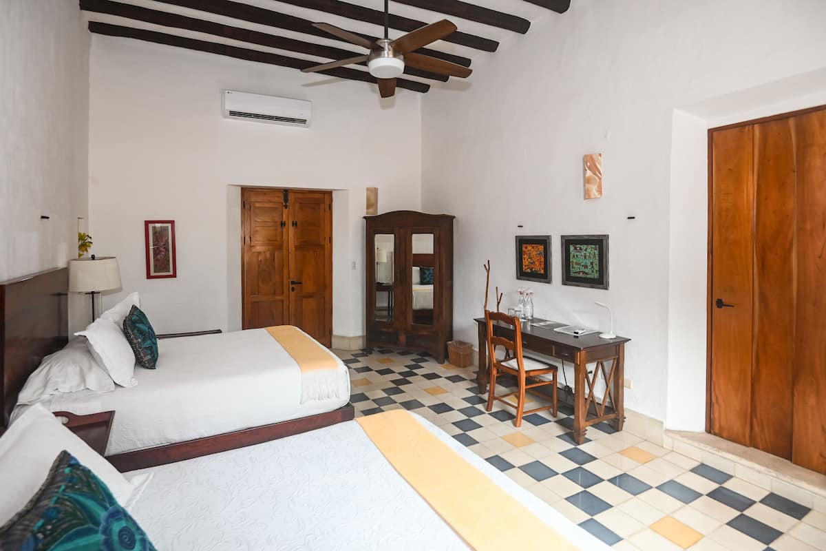 Quarto de hotel com cama, escrivaninha, cadeira, guarda-roupa e ventoinha no teto.