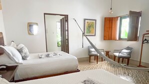 Una habitación de hotel con dos camas, una hamaca, una mesita y una silla.