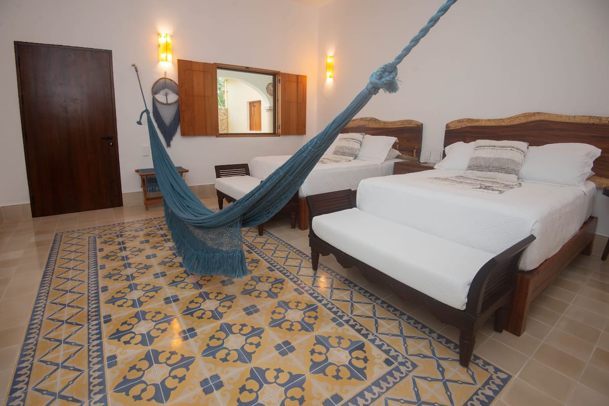 Quarto com duas camas, uma rede, piso estampado e porta de madeira.