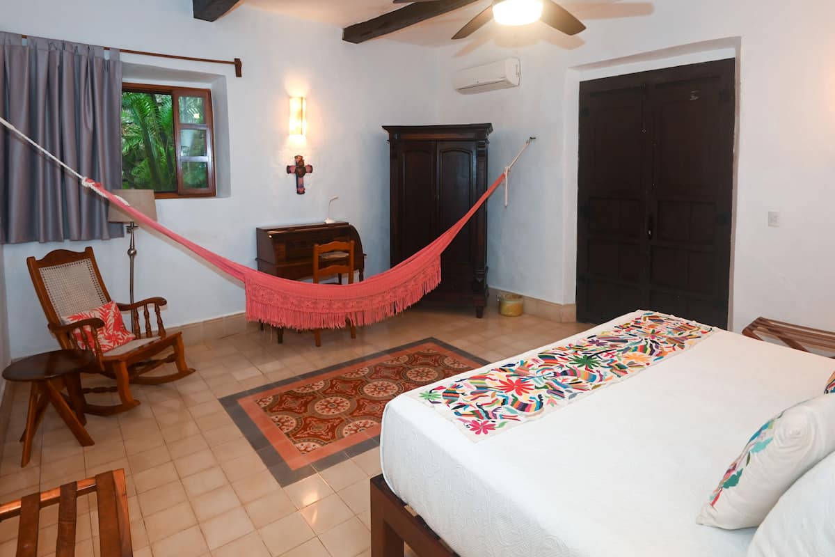 Quarto com cama, poltrona de balanço, escrivaninha, rede e porta.