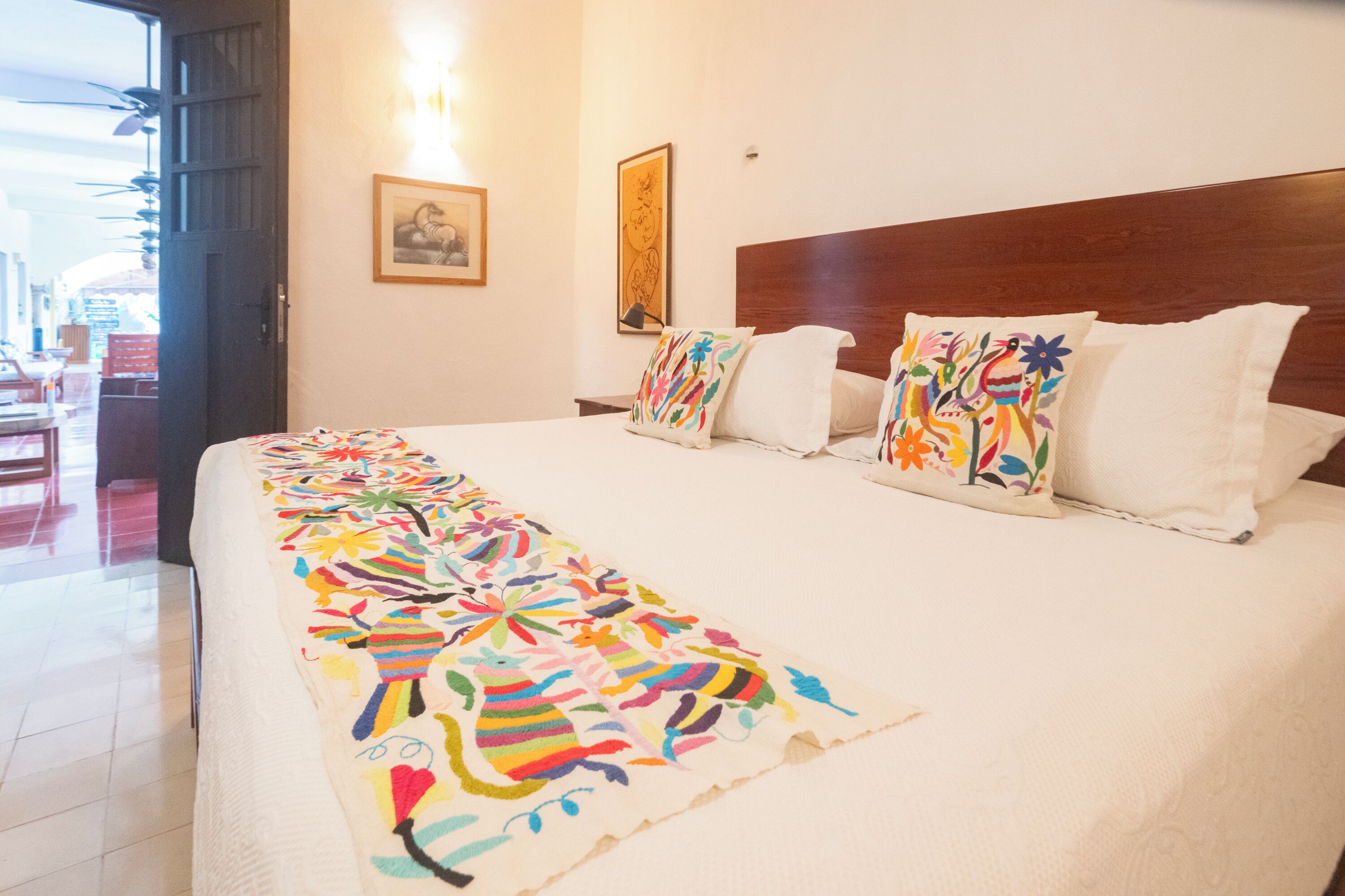 Habitación de hotel con una cama grande, almohadas coloridas y un mural en la pared.