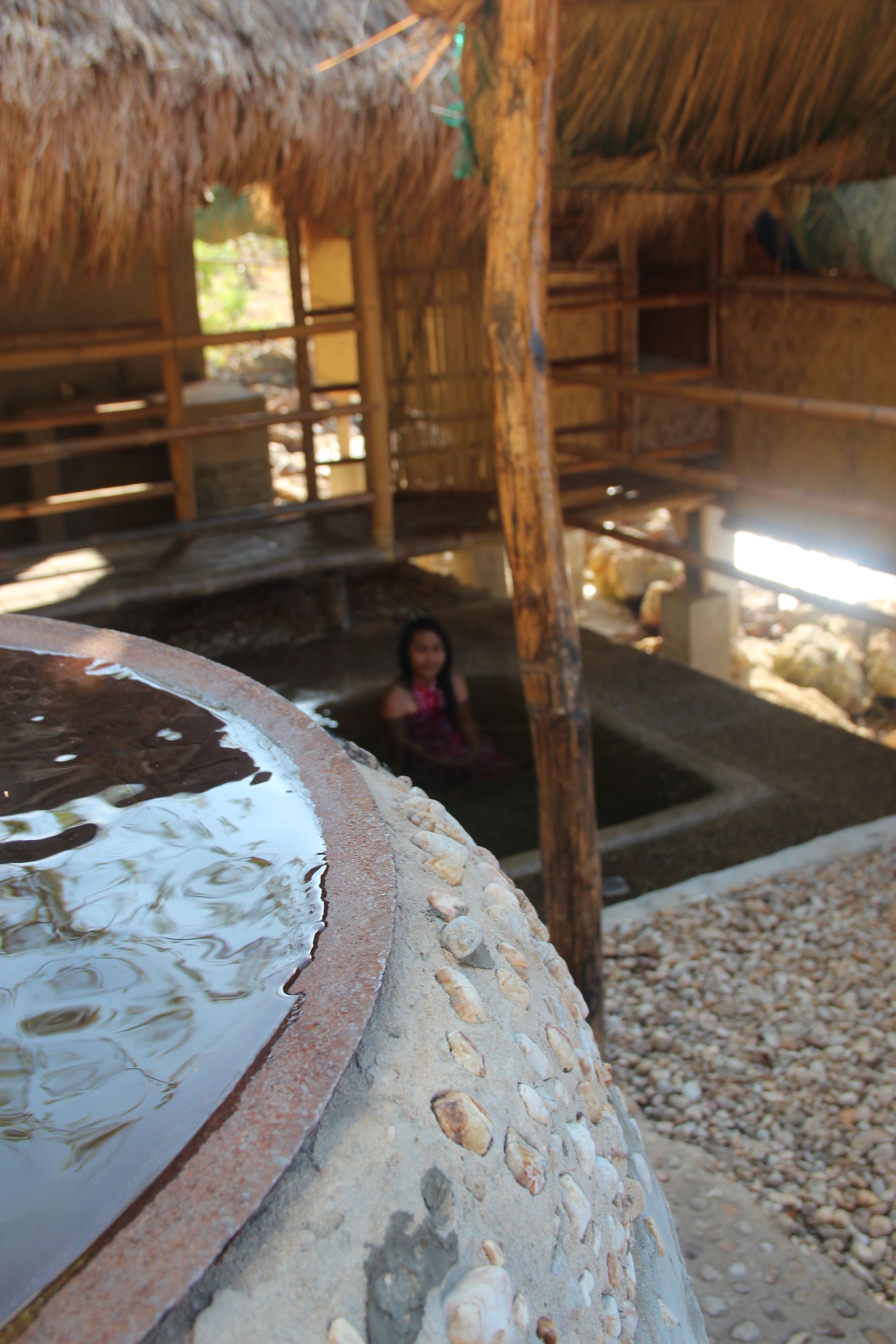 Una construcción rústica con techo de paja, una pila de piedra en primer plano y una persona al fondo.