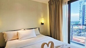 A hotel room with a large bed, a view of a cityscape through a window, and a wall-mounted light fixture.