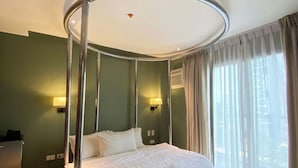 A modern hotel room with a circular bed, a desk, and a view of the city through large windows.