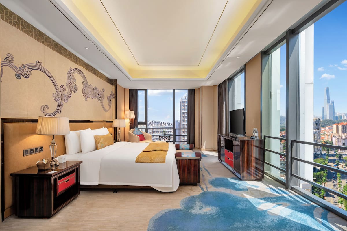 Een moderne hotelkamer met een groot bed, een bureau, een televisie en een balkon met uitzicht op de stad.