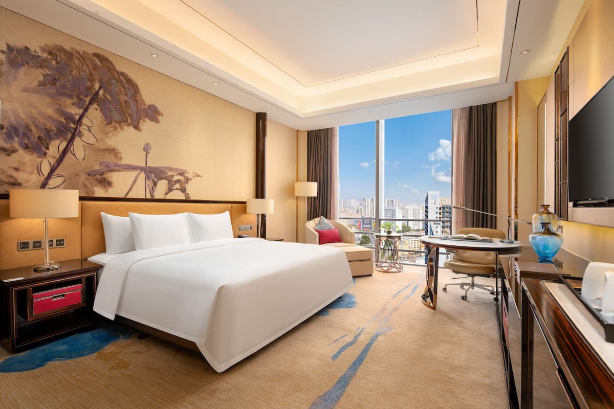 Een hotelkamer met een groot bed, een bureau, een stoel, een televisie en uitzicht op de stad.